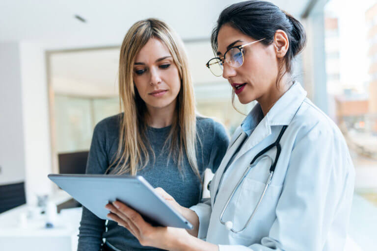 female primary care doctor talking while explaining medical treatment with digital tablet to patient in the consultation